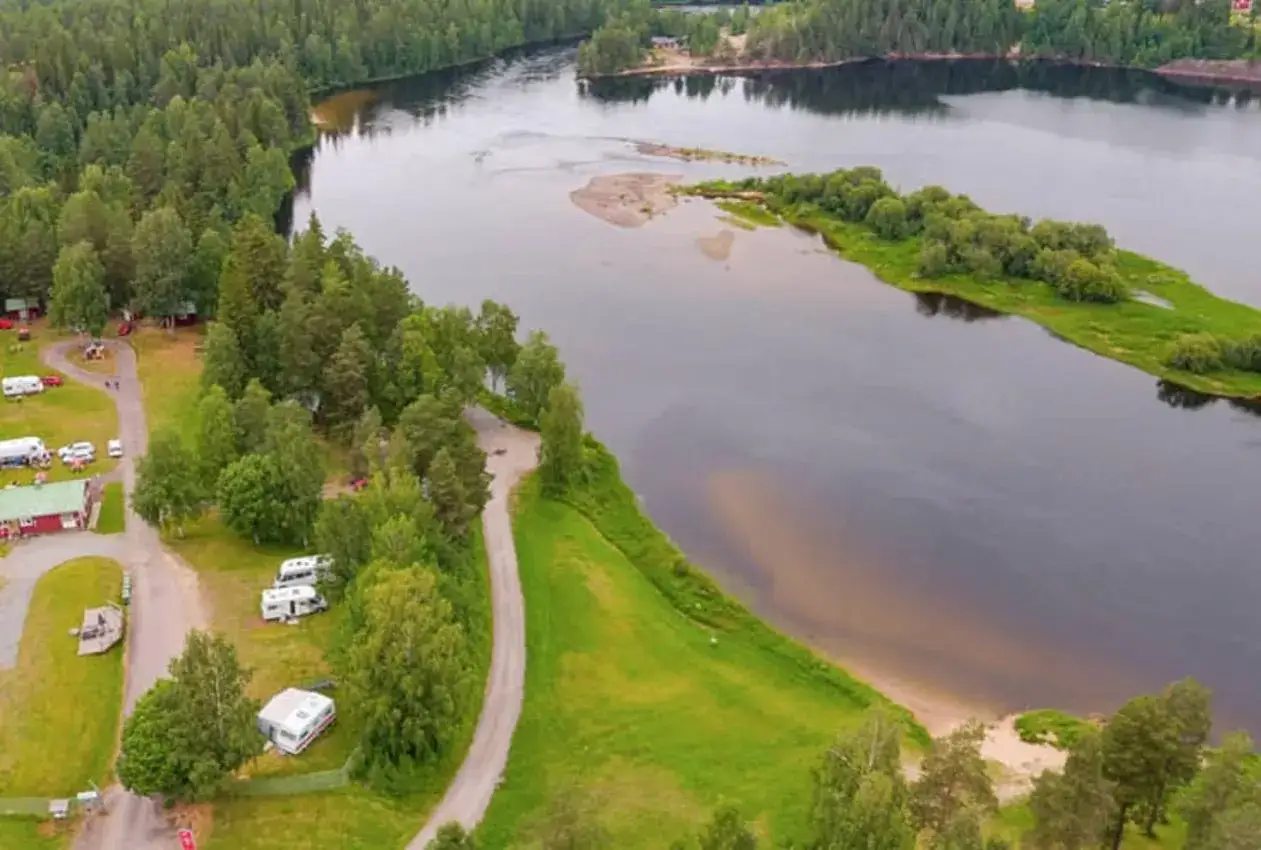 Vacker vy &ouml;ver Selholmens camping med husbilar och stugor vid en sj&ouml; omgiven av skog.