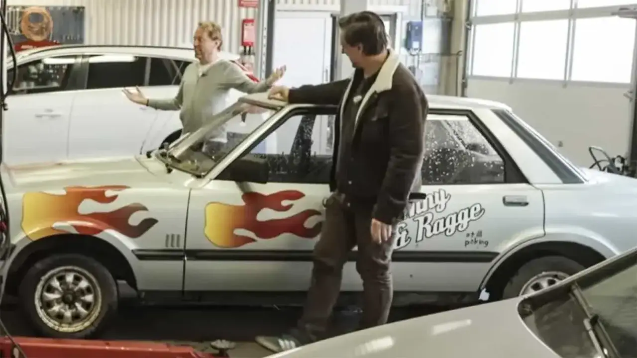 Tv&aring; m&auml;n vid en silverf&auml;rgad Ford med flammor p&aring; sidan. Texten 