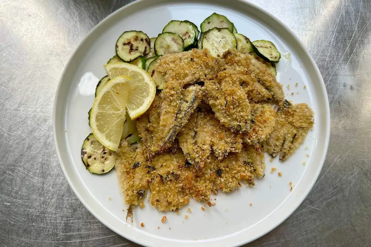 Alici al forno croccanti su un piatto bianco con zucchine grigliate e spicchi di limone.