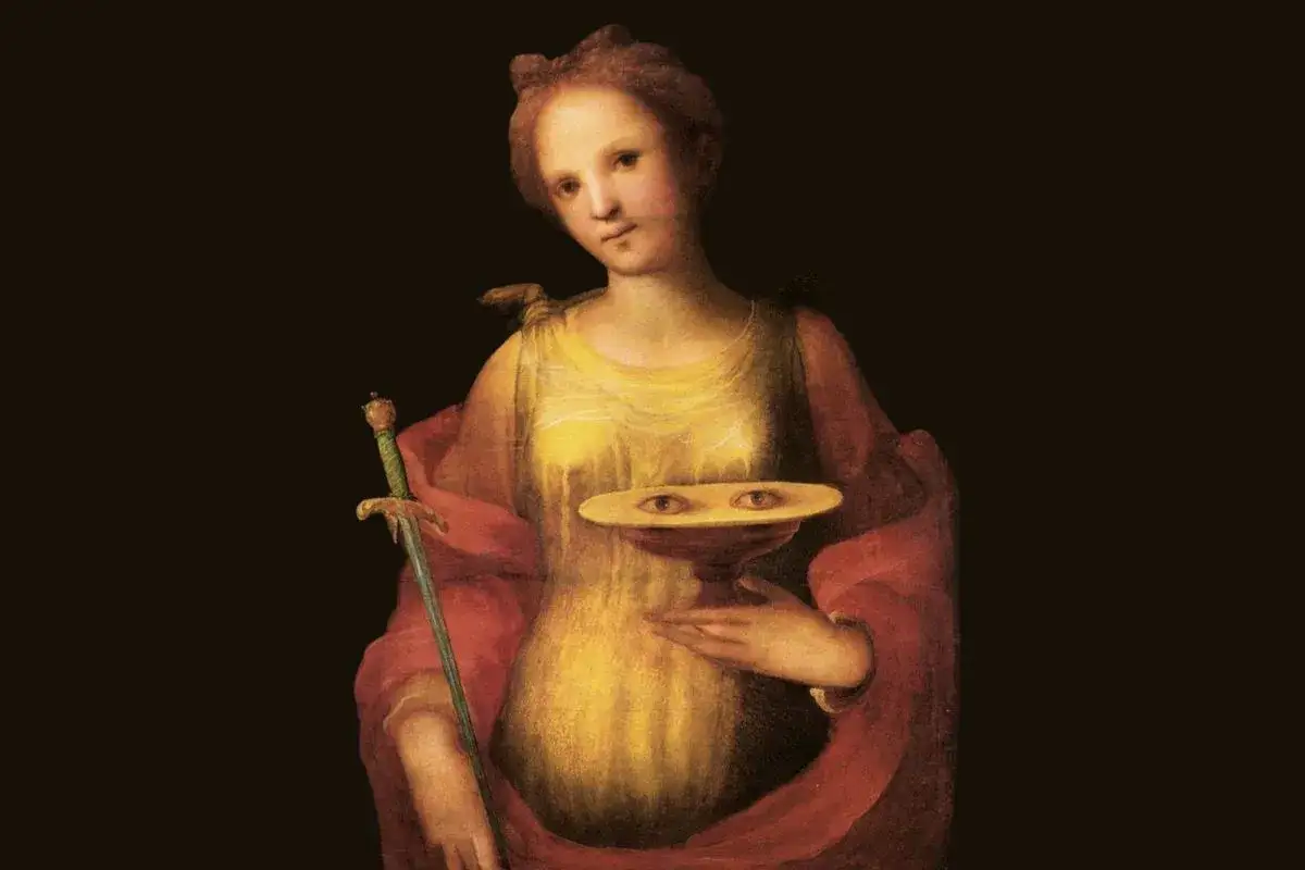 En kvinna i gul kl&auml;nning och r&ouml;d mantel h&aring;ller ett sv&auml;rd och en sk&aring;l med &ouml;gon. En fascinerande bild som visar hur Lucia s&aring;g ut enligt legenden.