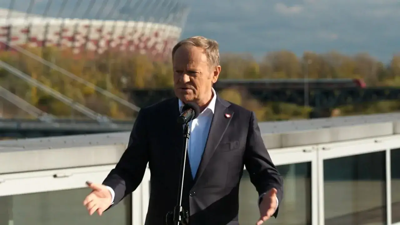 Donald Tusk w koninie przemawia na tle stadionu.