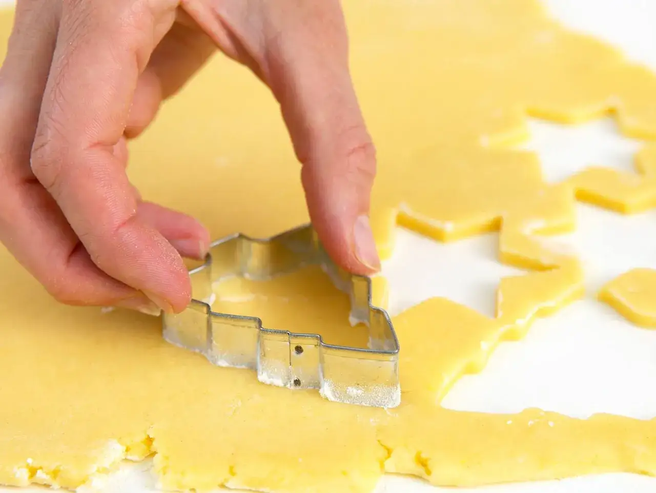 Hände formen mit einem Ausstecher Kekse aus Teig. Ein Schritt im butterkekse rezept für süße Leckereien.