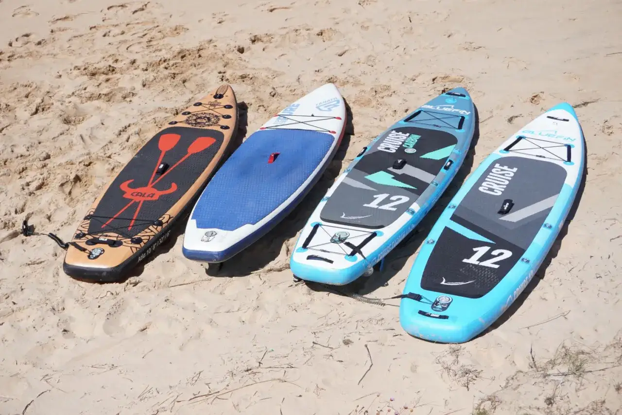Vier Stand Up Paddle Boards liegen im Sand. Das Gewicht der Boards variiert, was sie f&uuml;r unterschiedliche Paddler geeignet macht.
