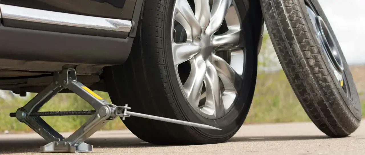 Un cric soul&egrave;ve une voiture pour changer un pneu crev&eacute;. La roue de secours est pr&ecirc;te.