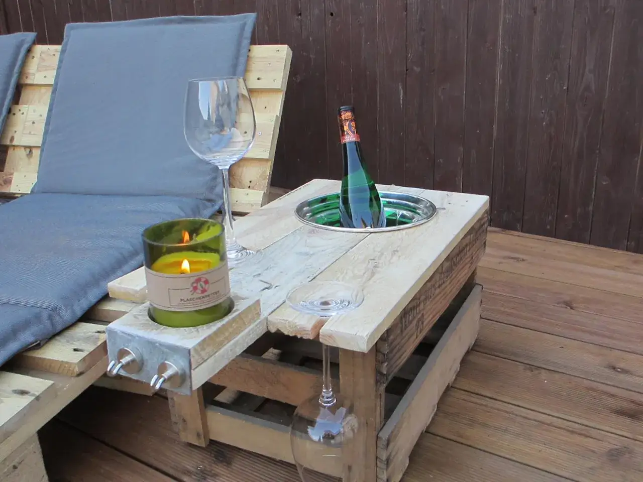 Kreative **Weinkisten Ideen**: Ein Tisch aus Weinkisten mit integriertem K&uuml;hler f&uuml;r eine Flasche Sekt, Kerze und Gl&auml;ser auf einer Holzterrasse.