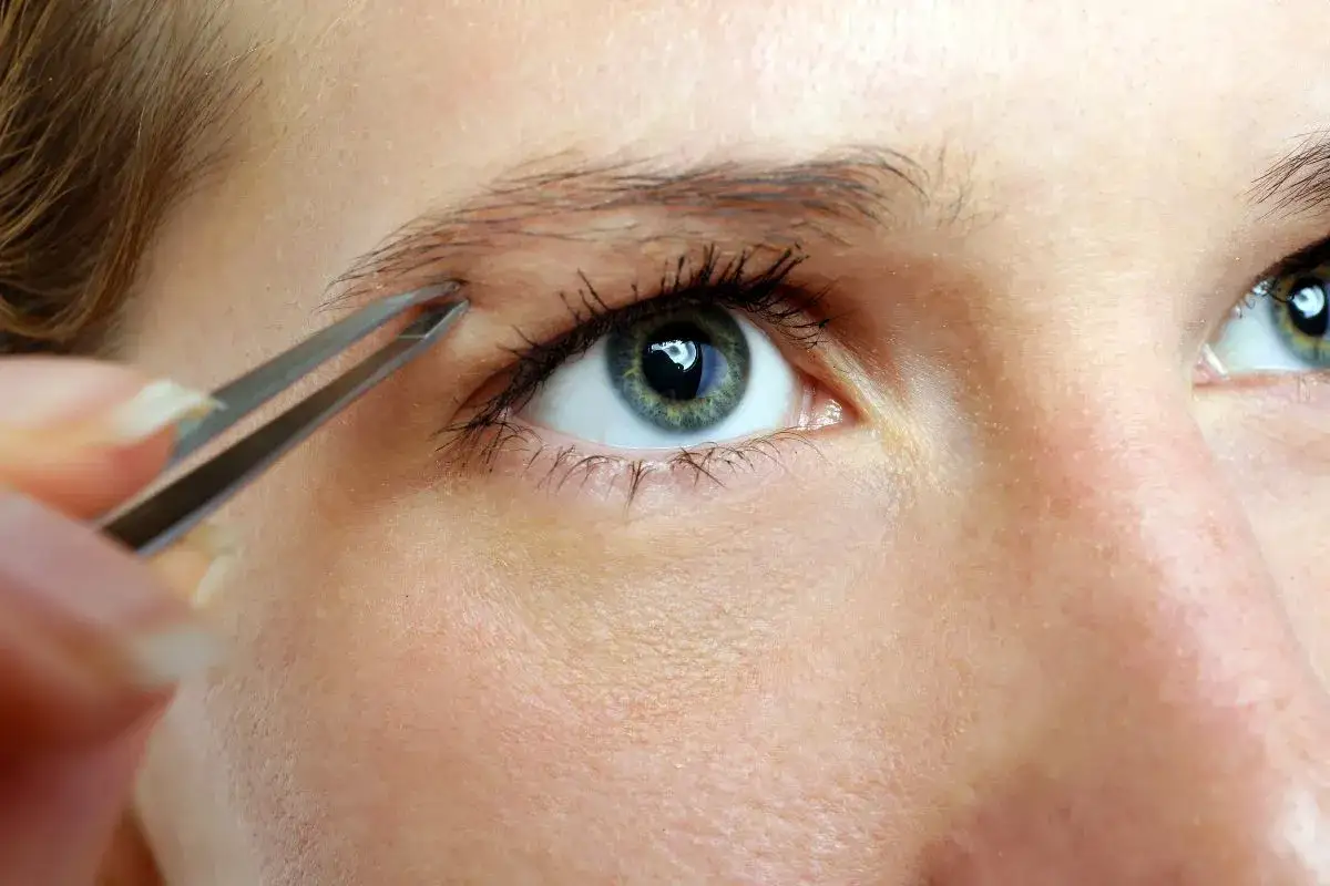 Une personne utilise une pince &agrave; &eacute;piler pour retirer un poil de son sourcil, peut-&ecirc;tre pour contrer une l&eacute;g&egrave;re alopecie sourcil.