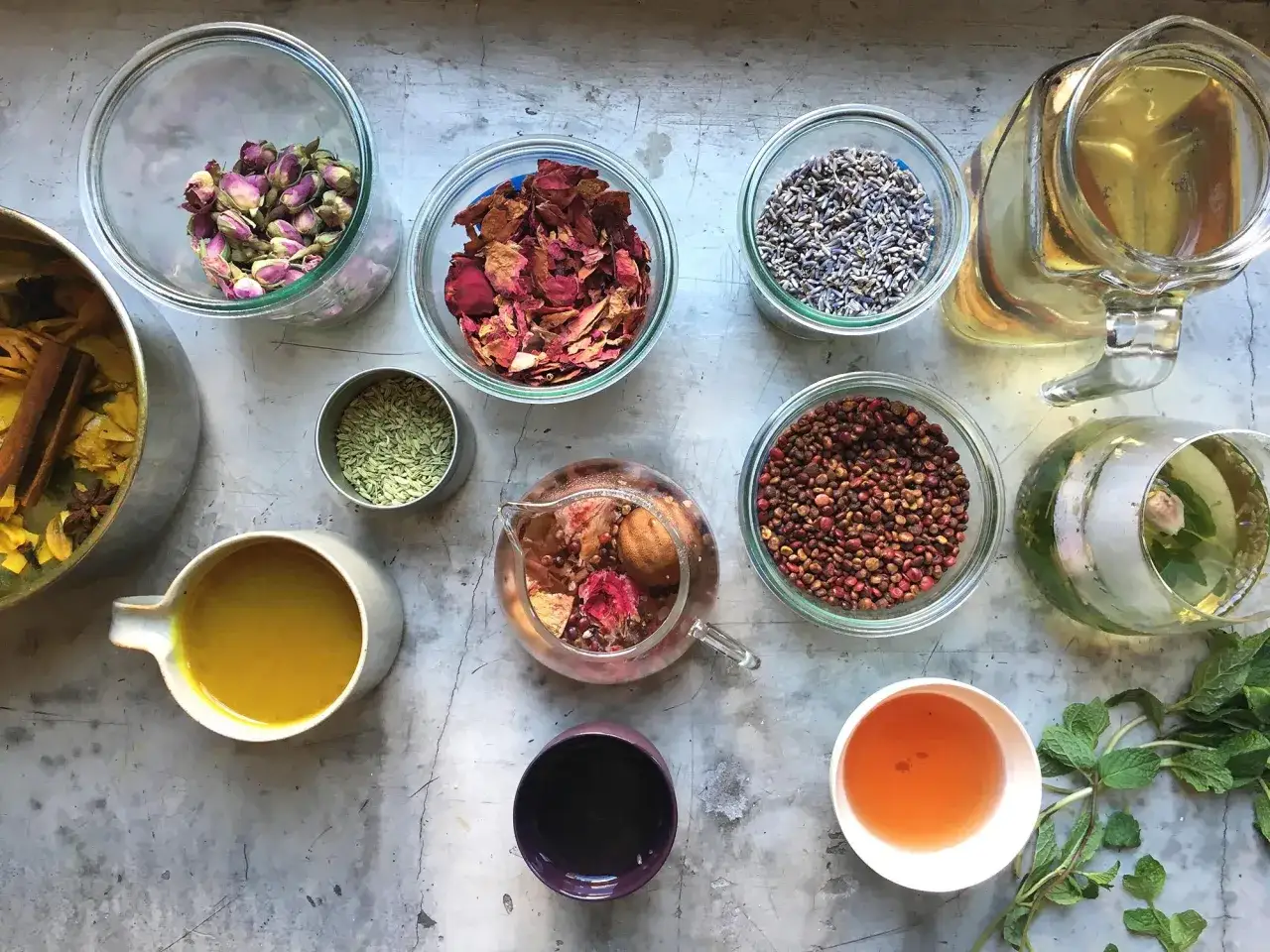 Pr&eacute;paration d'une infusion ayurv&eacute;dique : roses s&eacute;ch&eacute;es, lavande, fenouil, baies roses, menthe, et une tasse de liquide dor&eacute;.