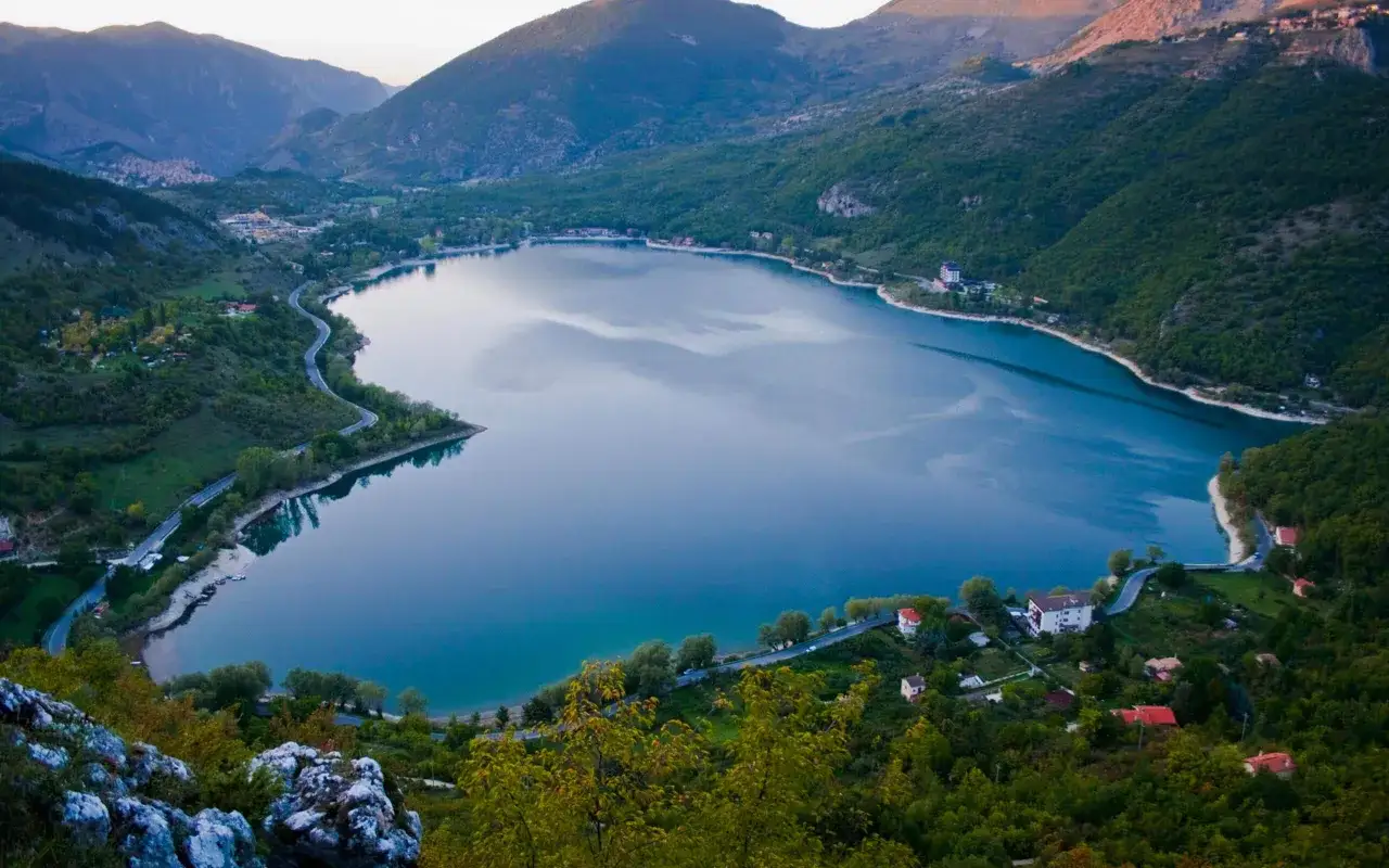 Un suggestivo lago a forma di cuore, incastonato tra montagne verdi e costeggiato da una strada tortuosa e piccoli borghi.