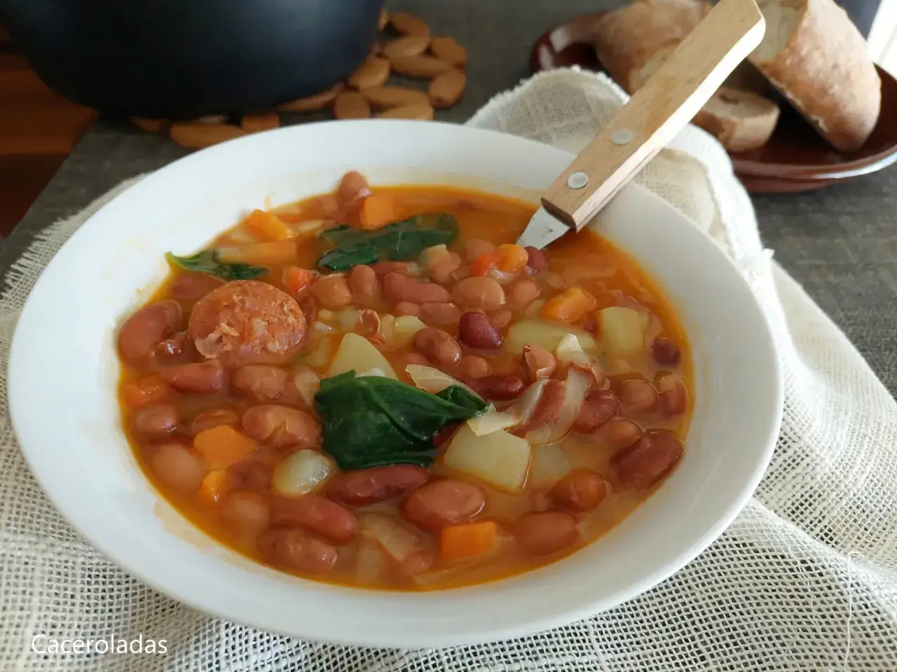 Un plato humeante de judías pintas con chorizo, patatas y espinacas, listo para ser disfrutado.