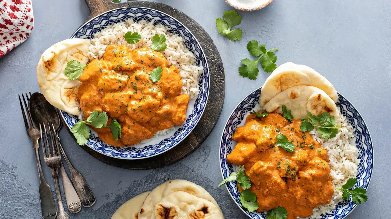 Pyszny Butter Chicken przepis: kremowy kurczak w sosie pomidorowym z ryżem basmati i chlebkiem naan, udekorowany świeżą kolendrą.