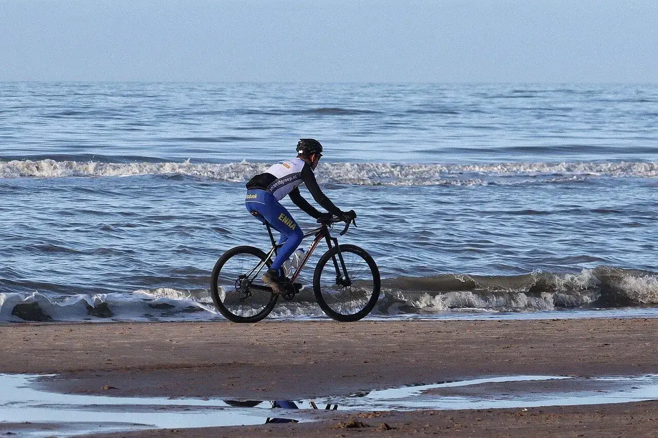Kolarz na rowerze pokonuje trasę rowerową Hel, jadąc brzegiem morza. Fale delikatnie obmywają koła.