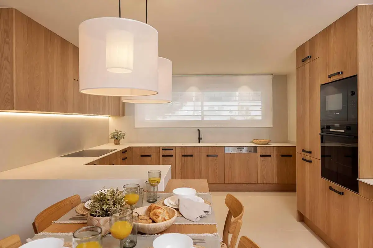 Cocina moderna con gabinetes de madera, encimera blanca y mesa de desayuno. Ideas para como diseñar una cocina funcional y elegante.