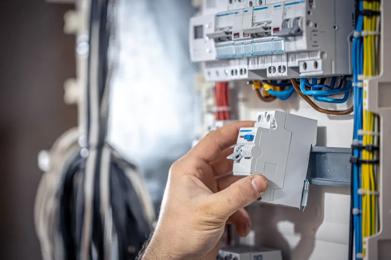 Elektryk dokonuje sprawdzania bezpiecznika miernikiem w skrzynce z przewodami.