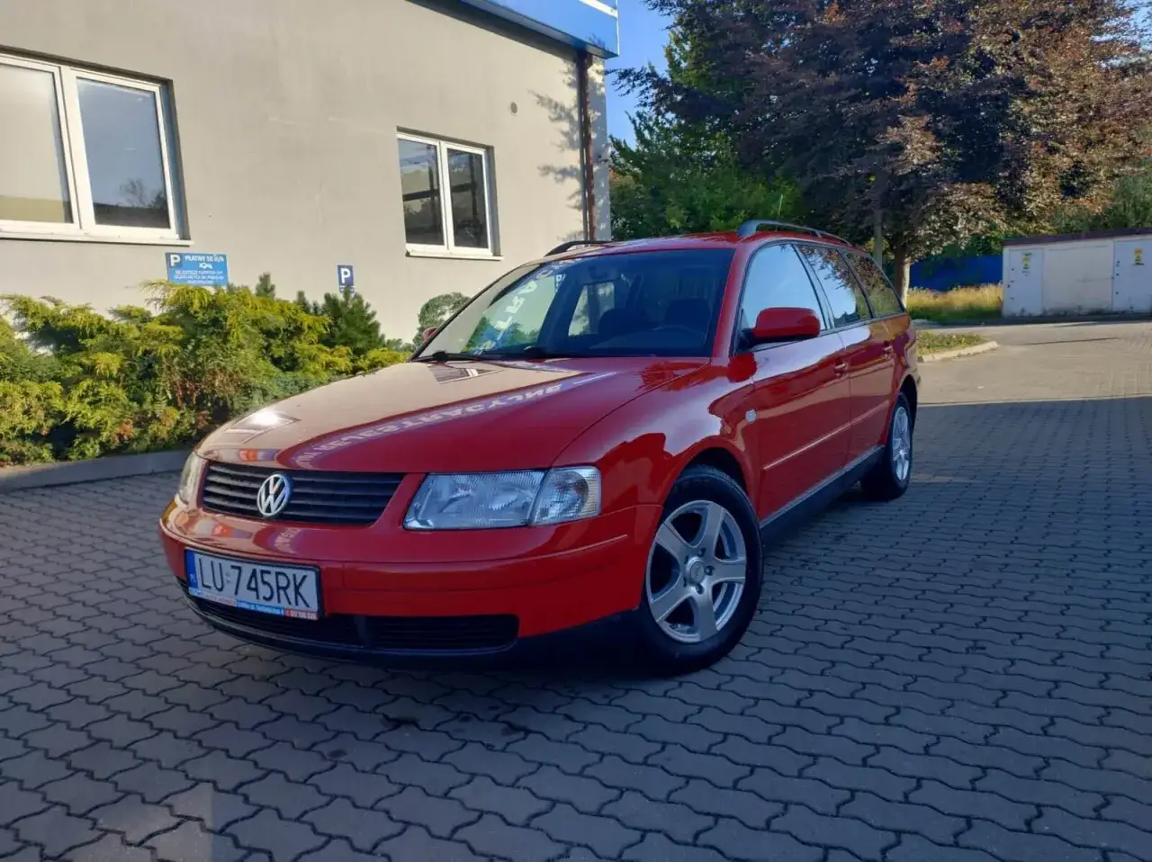 Czerwony Volkswagen Passat B5 kombi zaparkowany na kostce brukowej.