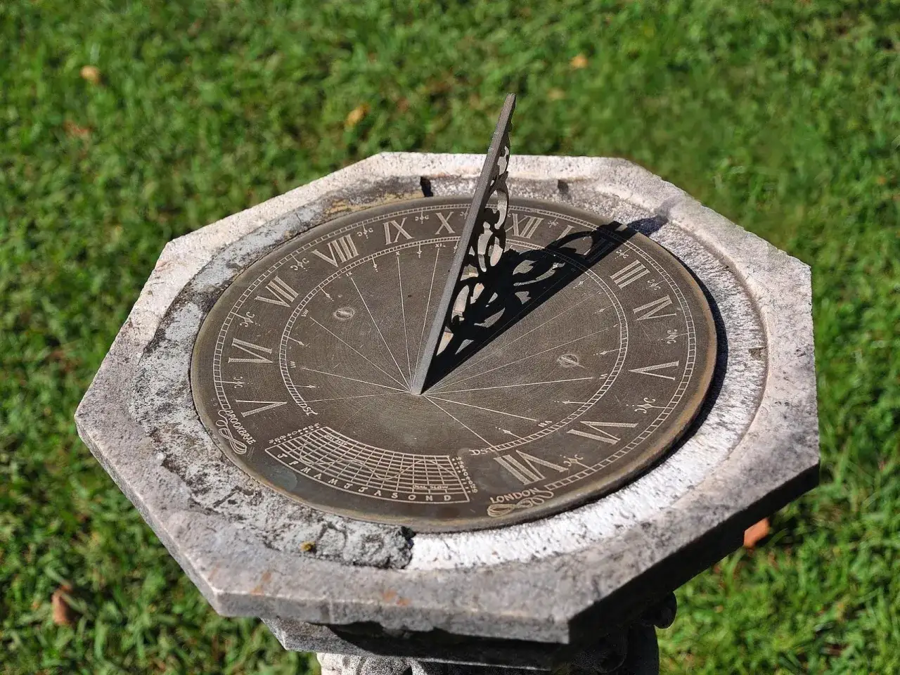 Reloj de sol antiguo con n&uacute;meros romanos y gnomon, ideal para orientarse con reloj de agujas en un jard&iacute;n soleado.