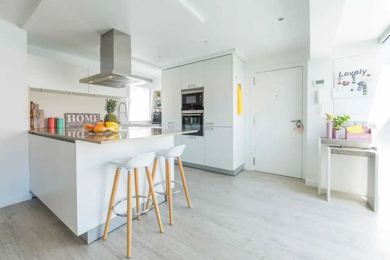 Cocina moderna con isla, taburetes y suelo de tarima AC5. Frutas frescas y decoración