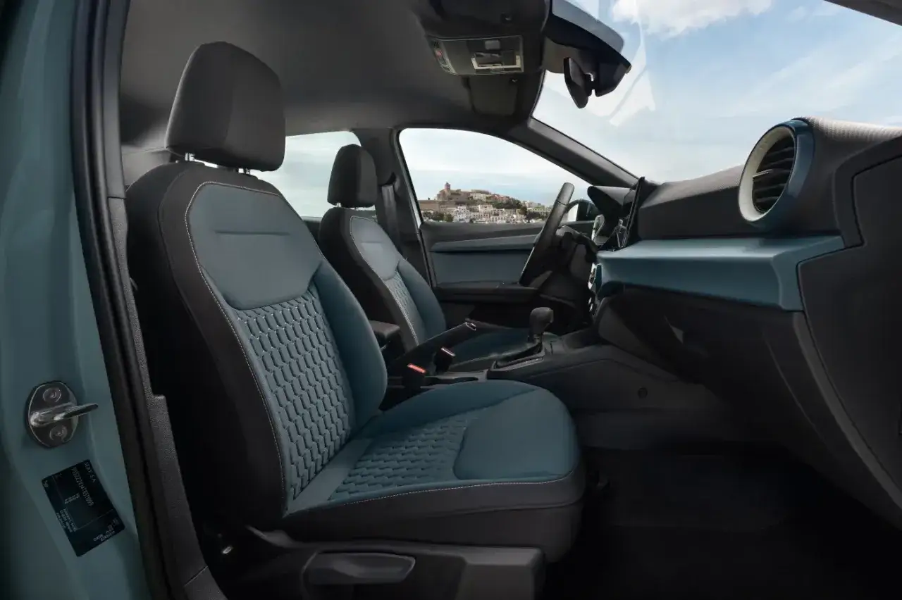 Wnętrze Seat Arona FR z niebieskimi, teksturowanymi siedzeniami i widokiem na miasteczko na wzgórzu.