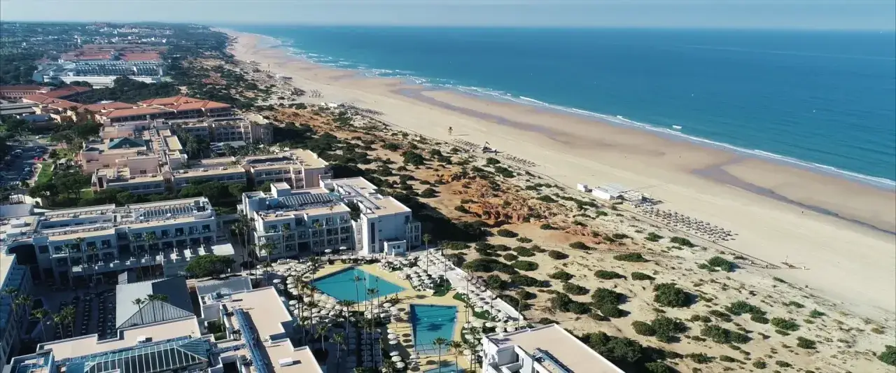 Luftaufnahme von Hipotels Barrosa Park mit Blick auf den Strand und das Meer. Mehrere Hotelgeb&auml;ude mit Pools und Sonnenschirmen sind zu sehen.