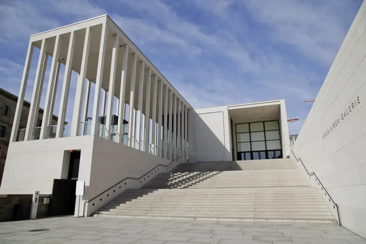Moderne, helle berlin architektur der James-Simon-Galerie mit langer Treppe und S&auml;ulengang vor blauem Himmel.