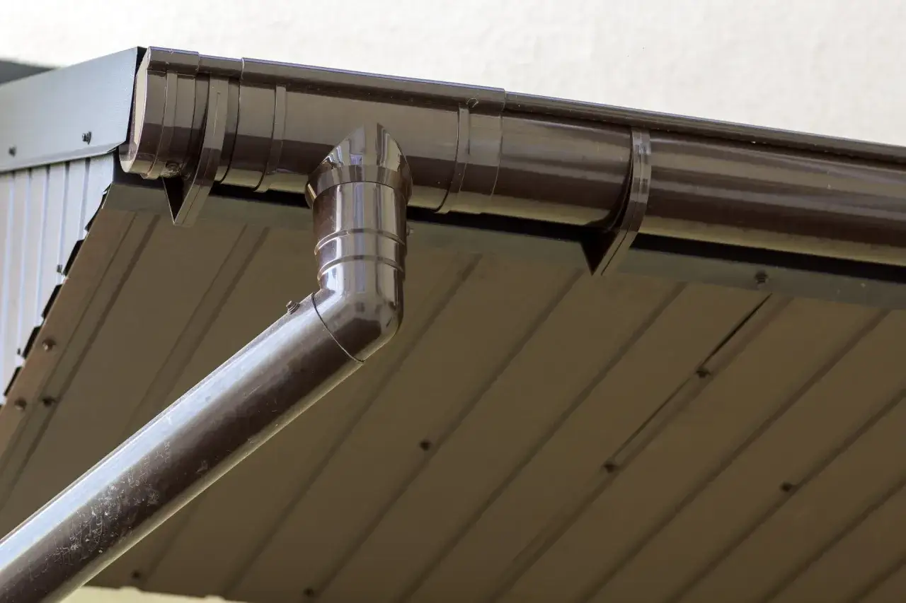 Brązowy montaż rynny plastikowej na altanie, odprowadzającej wodę z dachu.