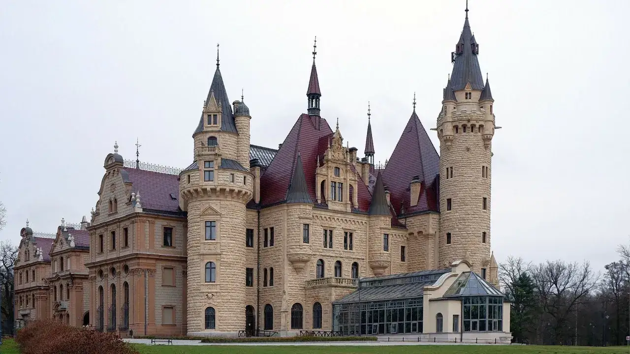 Zamek Książ, jeden z najpiękniejszych pałaców w Polsce, z licznymi wieżami i czerwonymi dachami, otoczony zielenią.