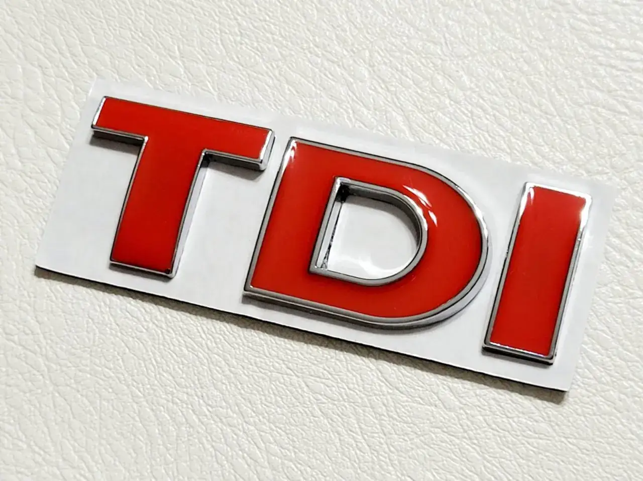 Czerwone oznaczenie TDI z chromowanym rantem, symbol silnika diesel.