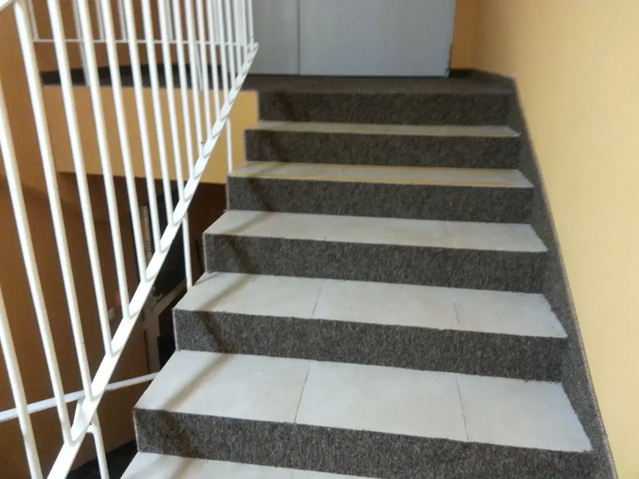 Nowe schody betonowe zyskały przytulny wygląd dzięki ciemnej wykładzinie. Biała poręcz dodaje elegancji.