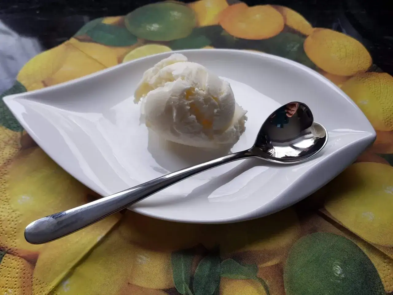 Ein Löffel cremiges Batida de Coco Eis auf einem Blatt-Teller, umgeben von Zitrusfrüchten.