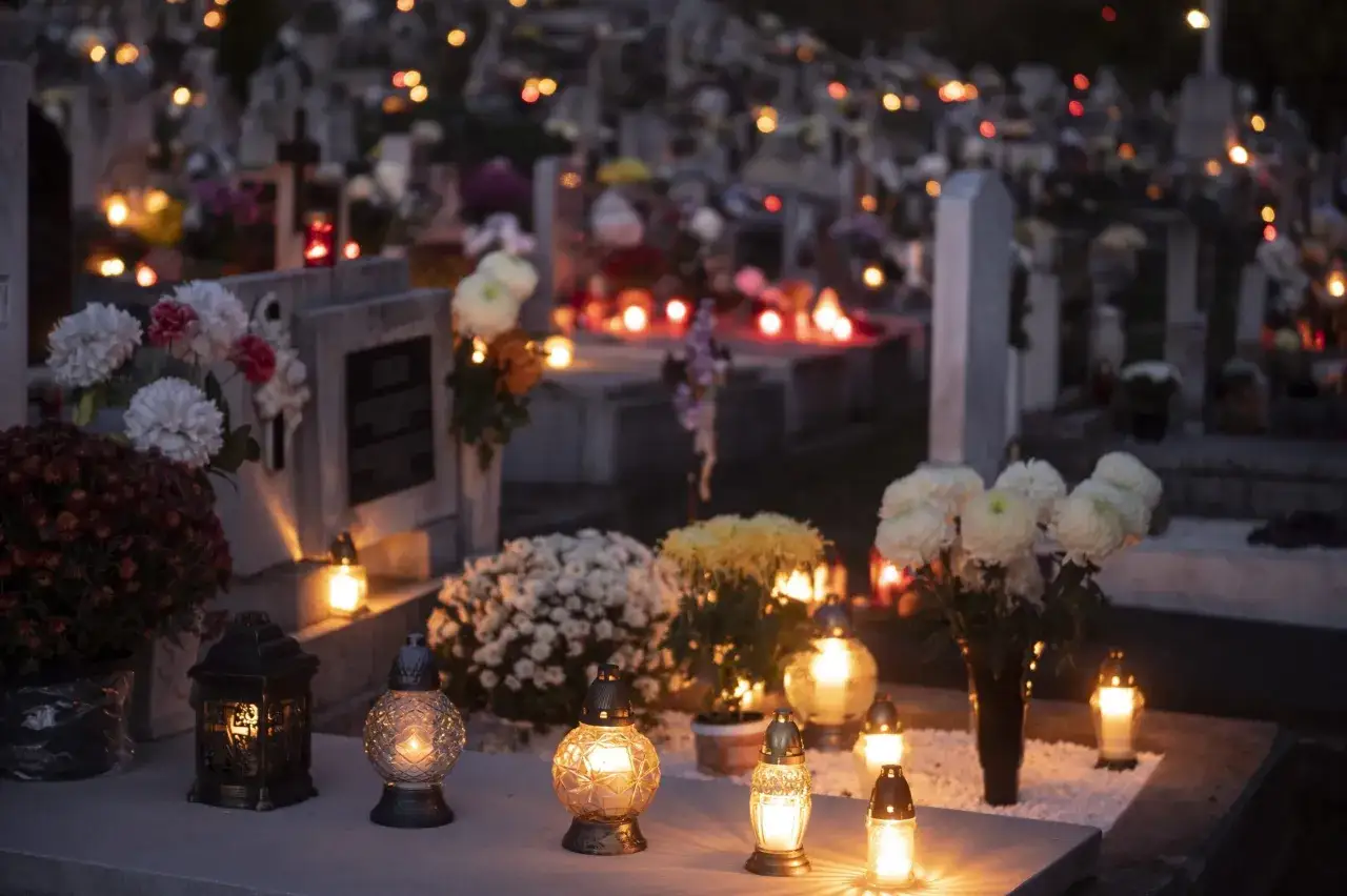 Grabsteine mit Blumen und Kerzenlicht im Dunkeln, eine Szene, die an Allerheiligen katholisch erinnert.
