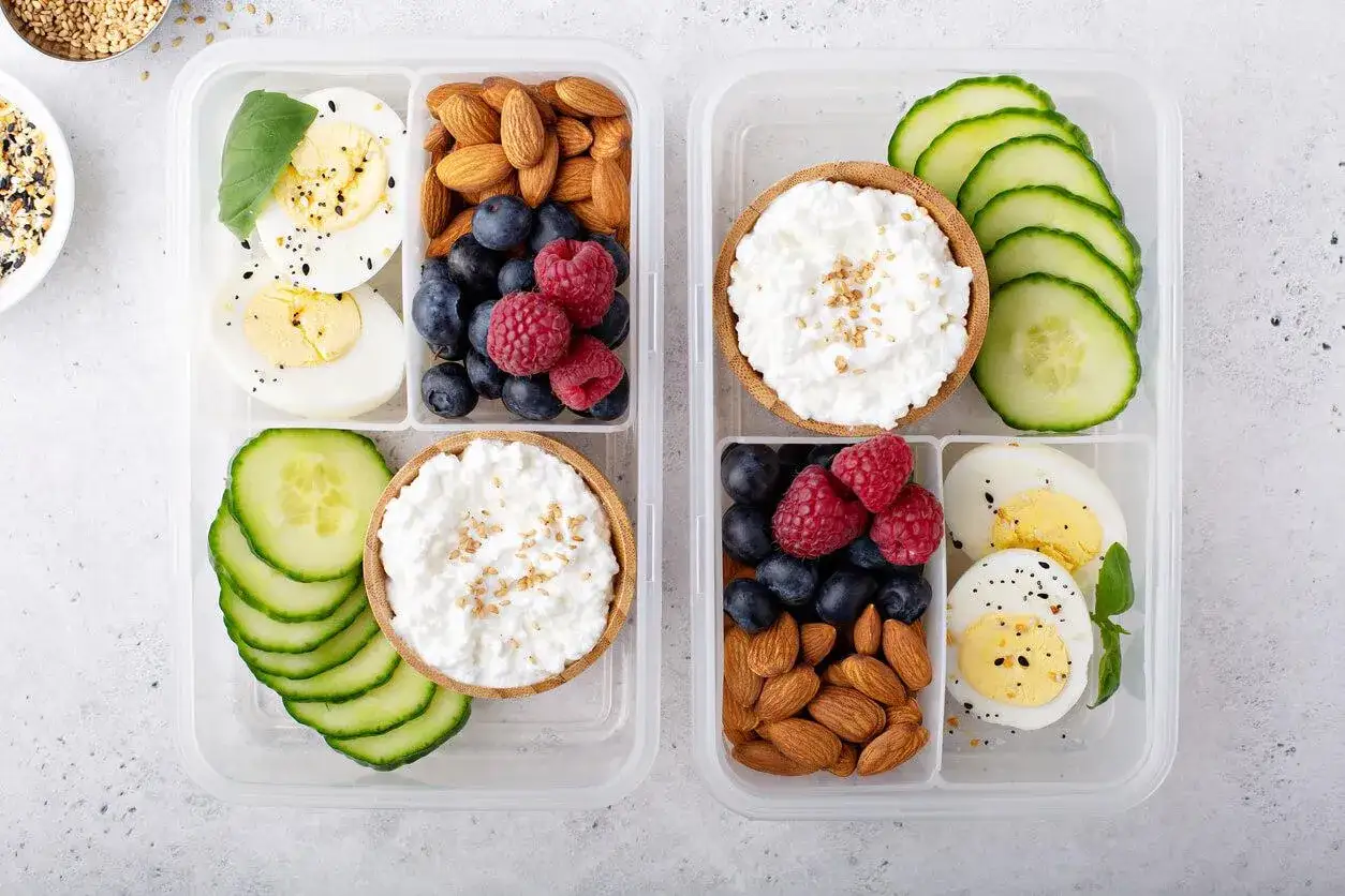 Zwei Bento-Boxen mit leckeren low carb snacks: Eier, Beeren, Mandeln, Gurken und Quark.