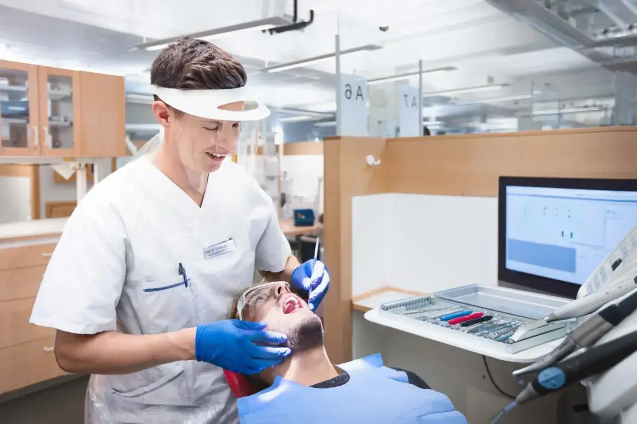 En person i skyddsutrustning utför en undersökning på en patient, en del av tandhygienist utbildning.