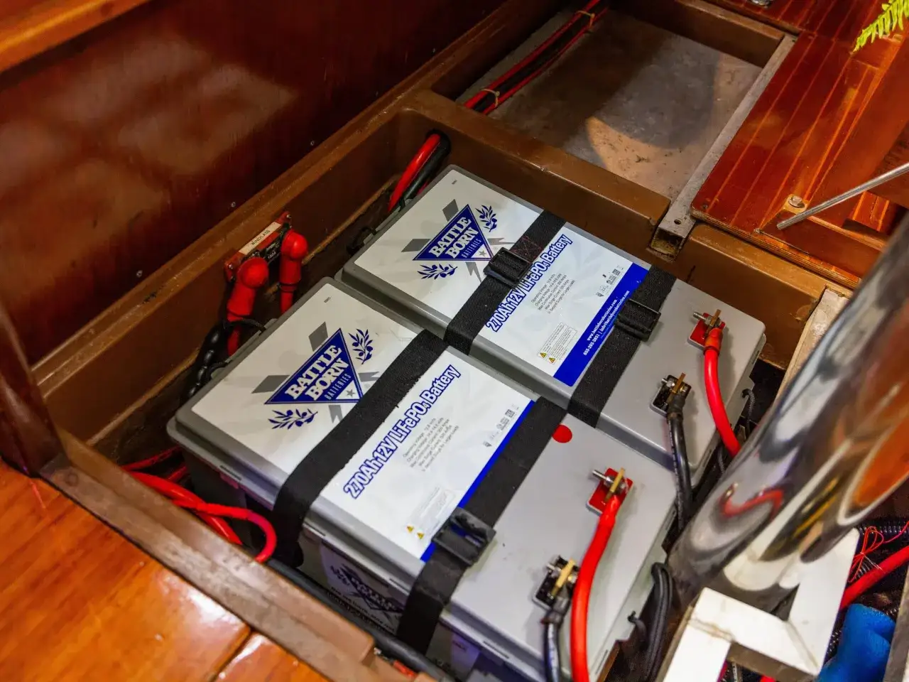 Due batterie LiFePO4 da 270Ah 12V, con cavi rossi e neri, installate in un vano in legno. Le batterie sono fissate con cinghie nere.