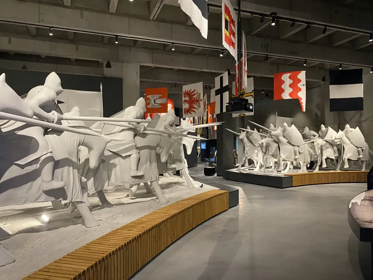 Białe rzeźby rycerzy na koniach, przypominające scenę z bitwy pod Grunwaldem, wiszące flagi historyczne.