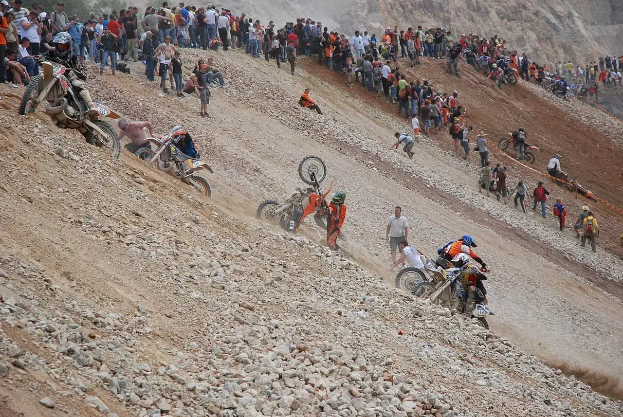 Widok na ekstremalny wyścig motocyklowy Erzberg Rodeo. Motocykliści walczą o każdy metr na stromym, kamienistym zboczu, a widzowie obserwują z góry.