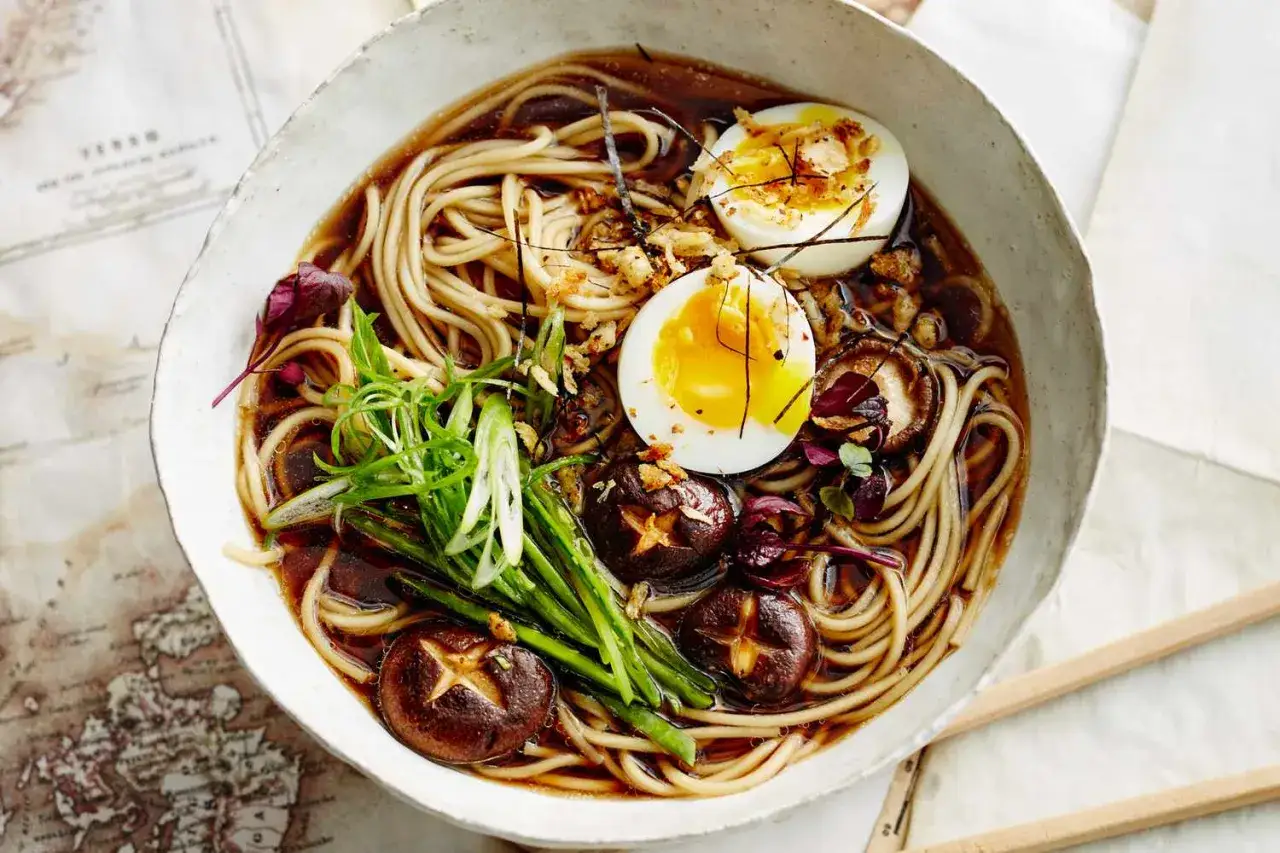 Miseczka aromatycznego ramen: makaron, jajko na pół, grzyby shiitake, szczypiorek i liście. Pyszne danie, które rozgrzewa.