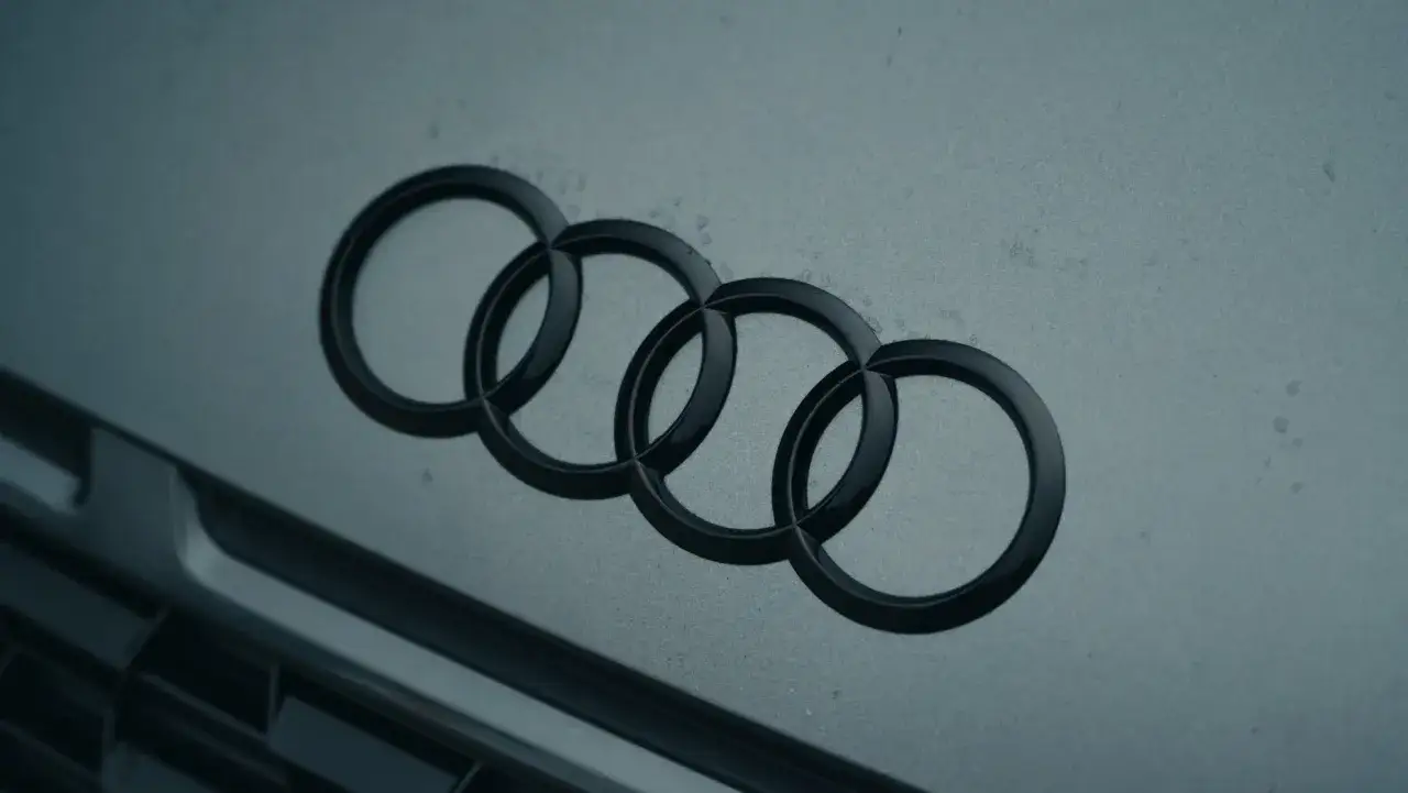 Cztery splecione pierścienie, symbol Audi, marki samochodów z Niemiec, błyszczą na szarym tle.