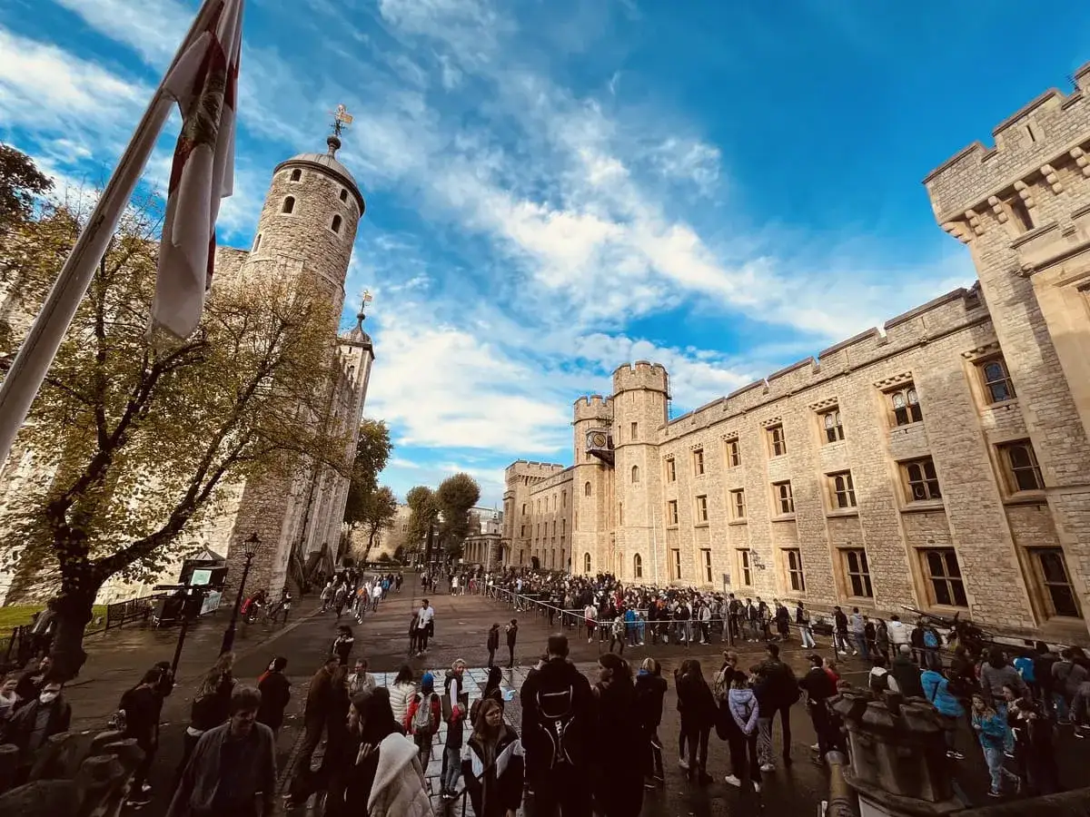 Tłum zwiedzających podziwia historyczną twierdza tower w słoneczny dzień. Flaga powiewa na maszcie obok kamiennej budowli.