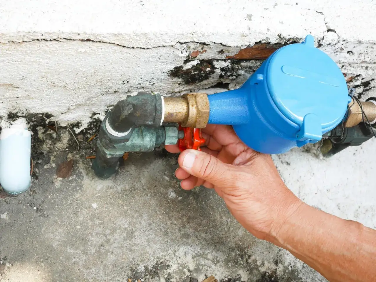 Main tenant ajuste le robinet rouge du compteur d'eau bleu, une étape clé pour la reparation fuite d'eau.