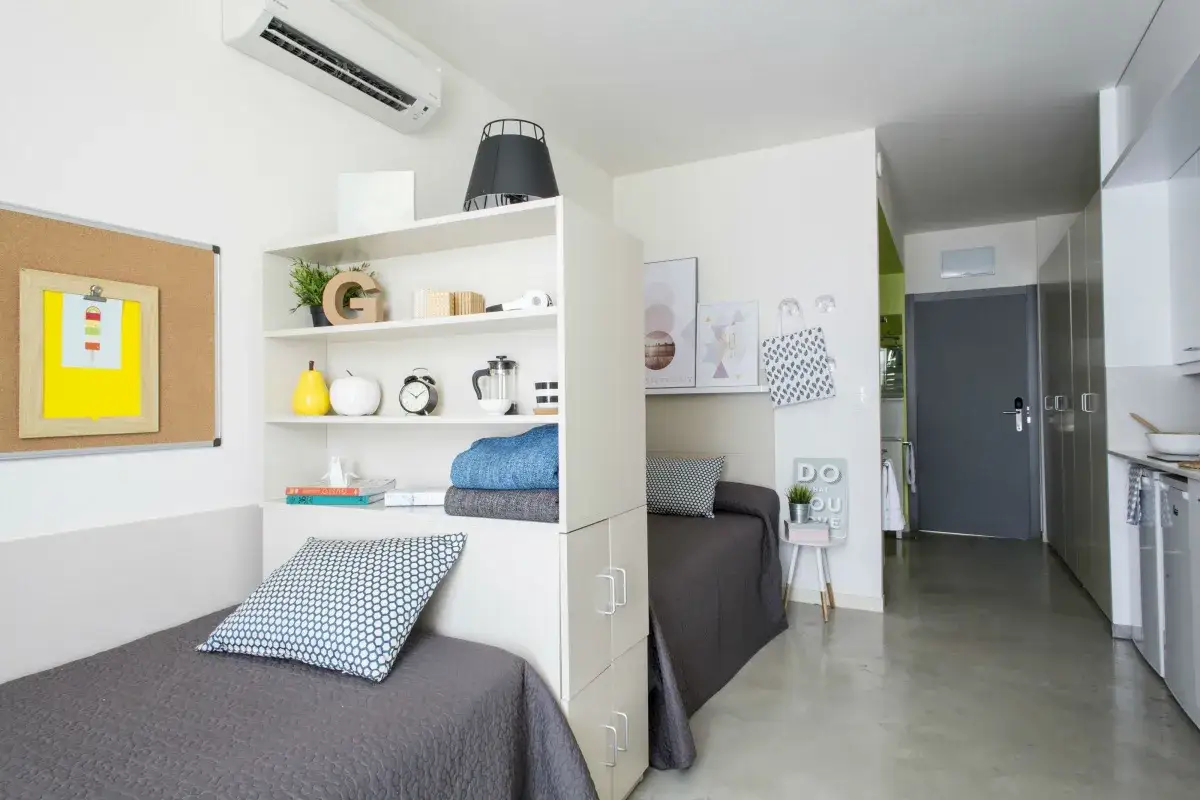 Habitaci&oacute;n en residencia la salle con dos camas, estanter&iacute;as y un peque&ntilde;o rinc&oacute;n de cocina.
