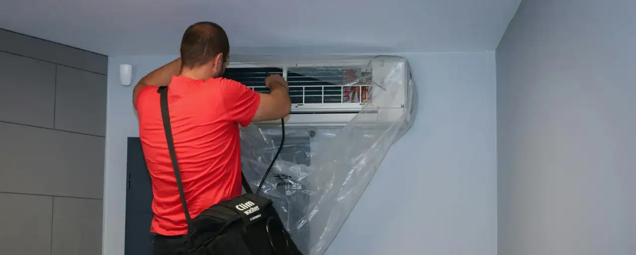 Technicien effectuant l'entretien d'une climatisation murale, une tâche essentielle pour tout locataire ou propriétaire soucieux de son confort.