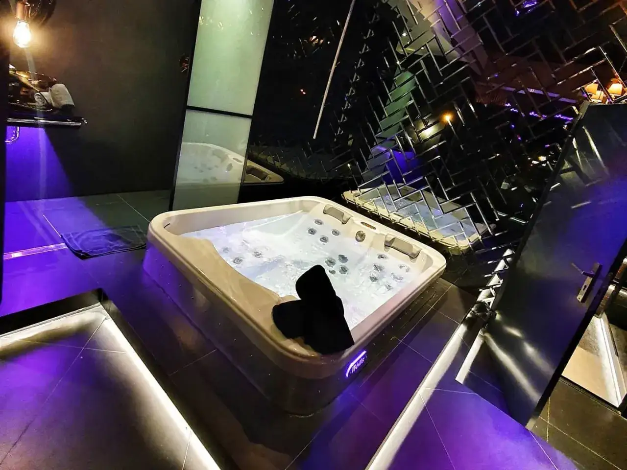 Luksusowa wanna z hydromasażem w hotelu Ramka Poznań, otoczona fioletowym światłem i lustrzanymi płytkami.