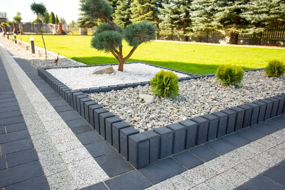 Nowoczesna palisada przy tarasie, otaczająca rabaty z kamieniami i miniaturowym drzewkiem.