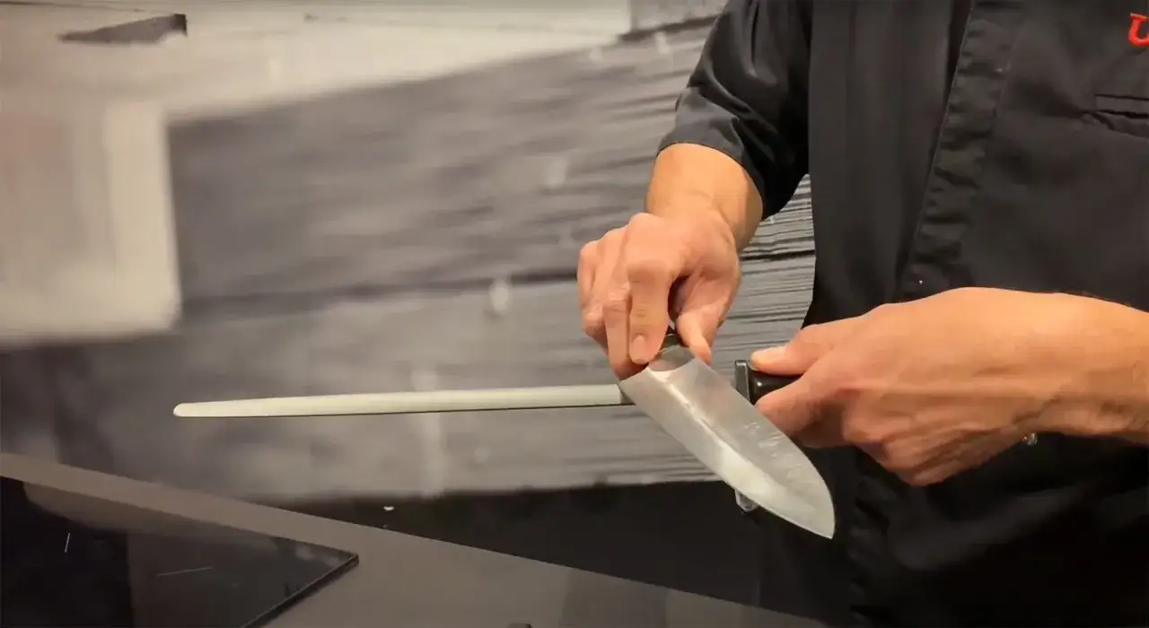 Un chef afila un cuchillo sobre una chaira, manteniendo el filo perfecto para cortar.