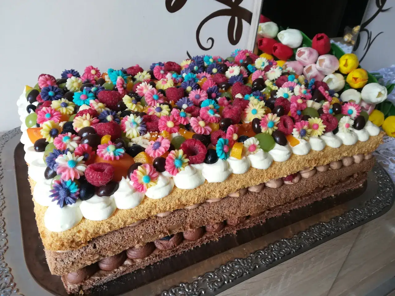Kolorowy tort udekorowany masą owoców i cukrowych kwiatków. Wygląda jak dzieło sztuki!