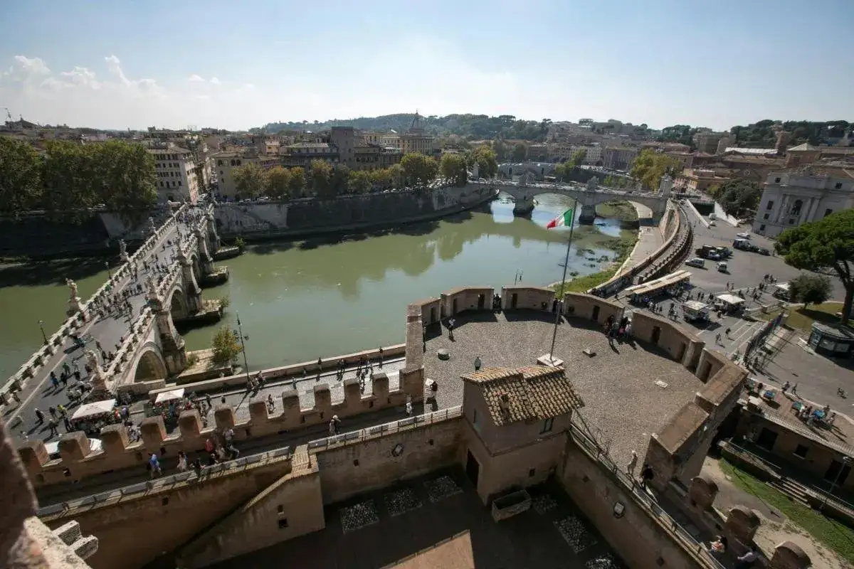 Widok na rzekę w Rzymie z mostem Ponte Sant'Angelo i Zamkiem Świętego Anioła. W tle widać włoską flagę.