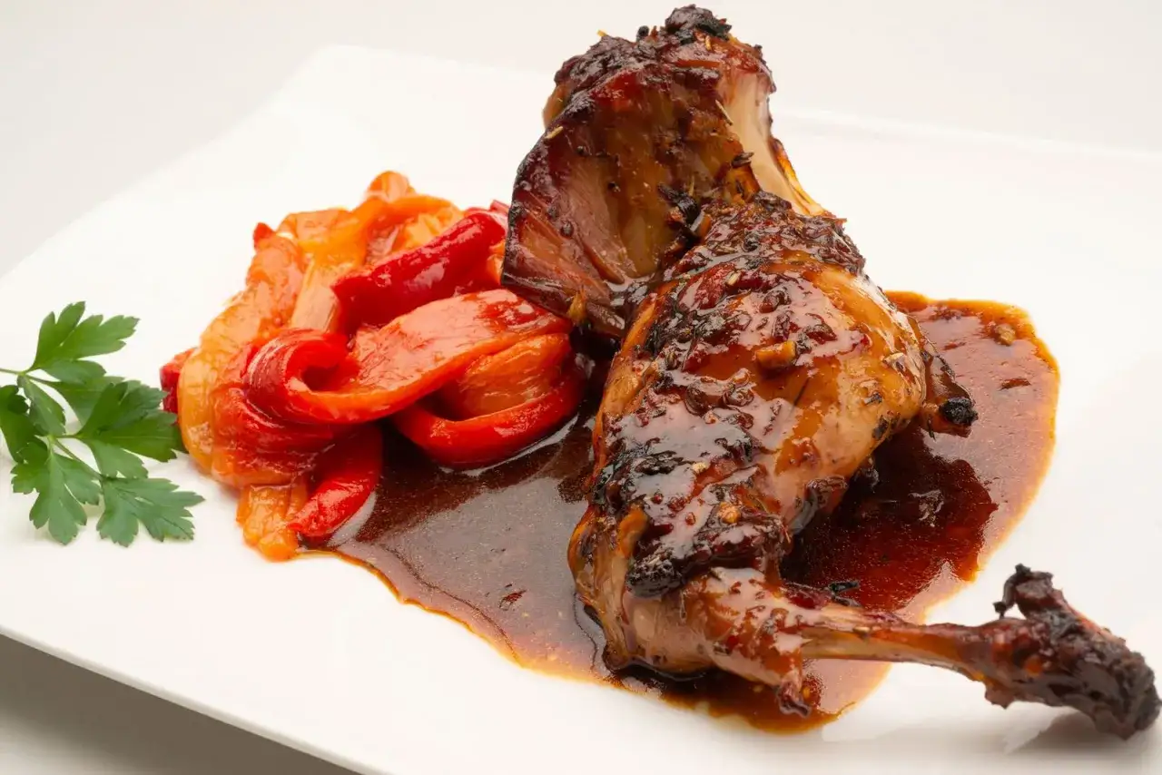 Delicioso conejo al horno ba&ntilde;ado en salsa, acompa&ntilde;ado de pimientos asados y perejil fresco.