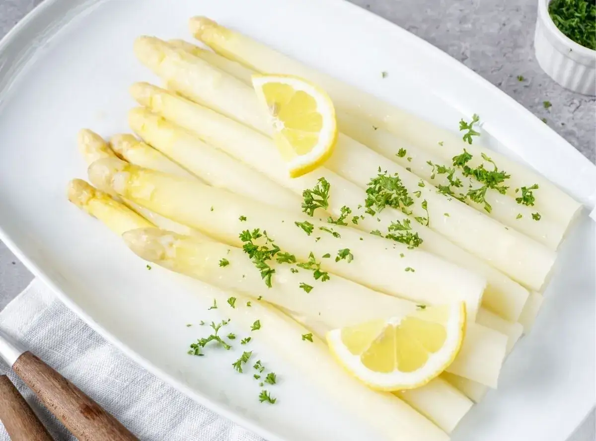 Frischer weißer Spargel, garniert mit Petersilie und Zitronenspalten, bereit für die Zubereitung.
