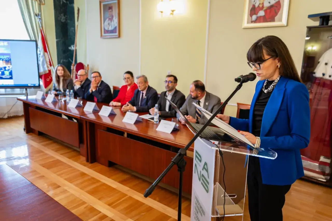 Prezentacja na temat stosunki międzynarodowe studia. Kobieta w niebieskiej marynarce przemawia do zebranych przy długim stole.