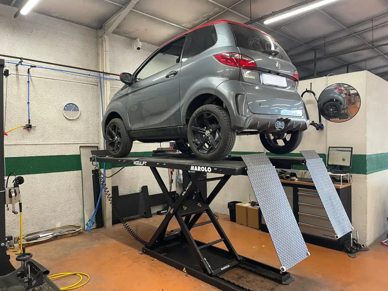 Une voiture sans permis grise sur un pont élévateur dans un garage. Une nouvelle loi sur les voitures sans permis pourrait rendre ces véhicules plus accessibles.