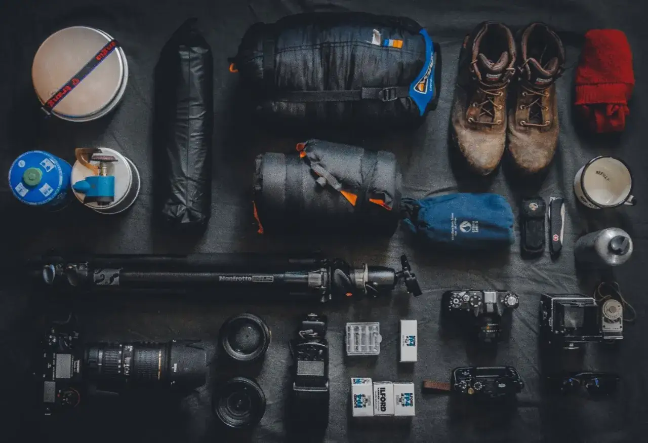Sprzęt do fotografii podróżniczej: śpiwór, buty, aparat, obiektywy, statyw, kuchenka turystyczna, kubek i inne akcesoria.